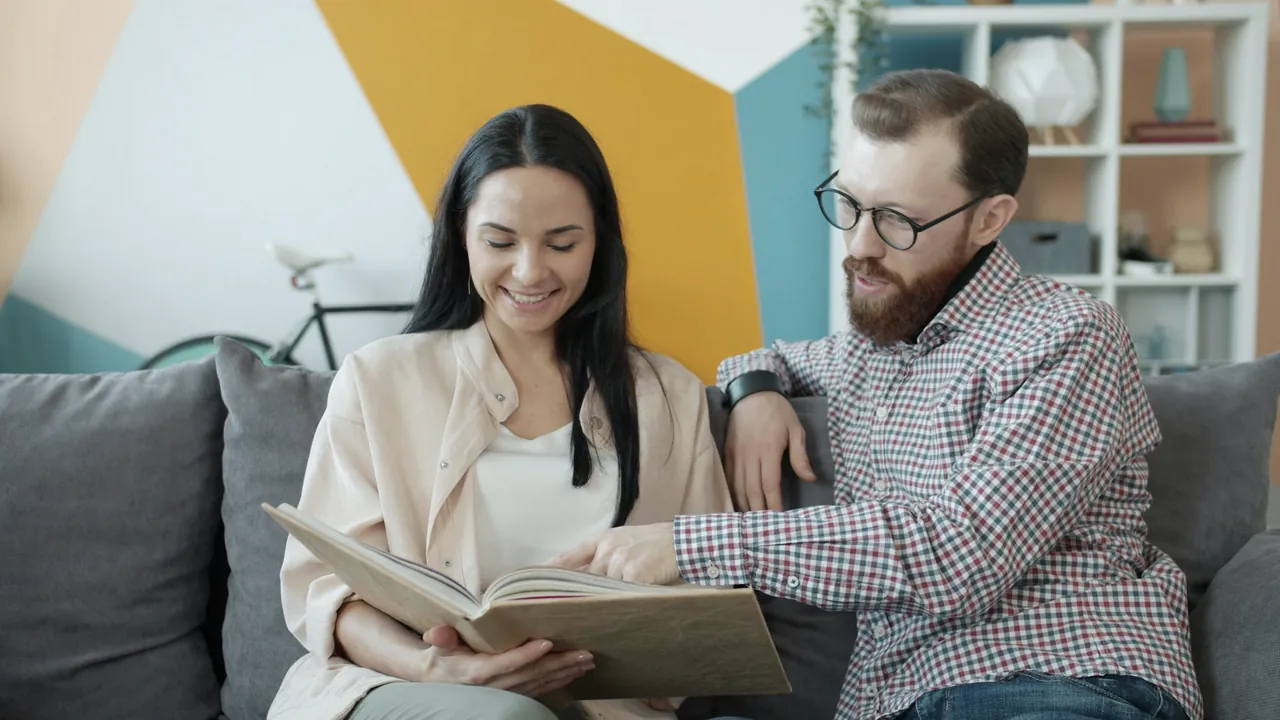 A couple sitting together on a sofa, looking through a photo album