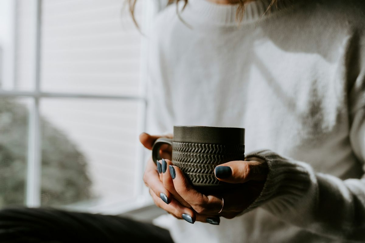 A person holding a warm mug in both hands beside a window