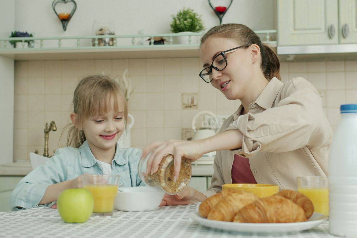 A parent and child eating breakfast together at a kitchen table