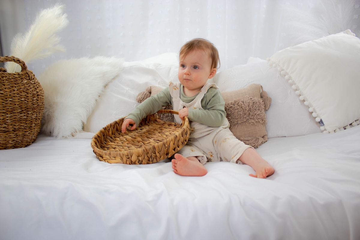 A baby sitting on a bed holding a basket