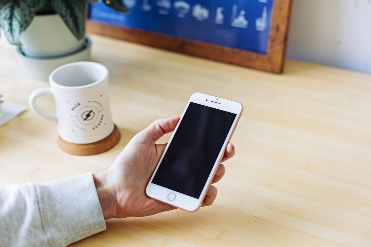 A person holding a phone beside a mug on a light desk