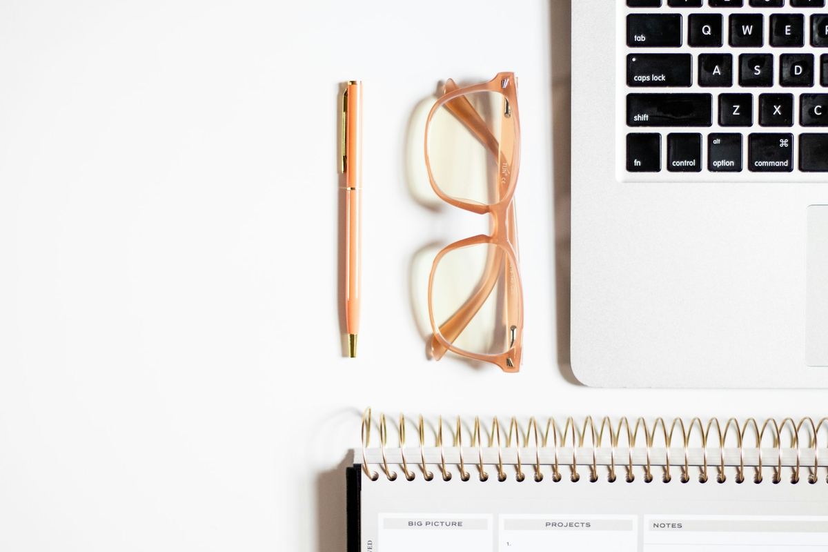 A desk with a laptop, glasses and a notepad