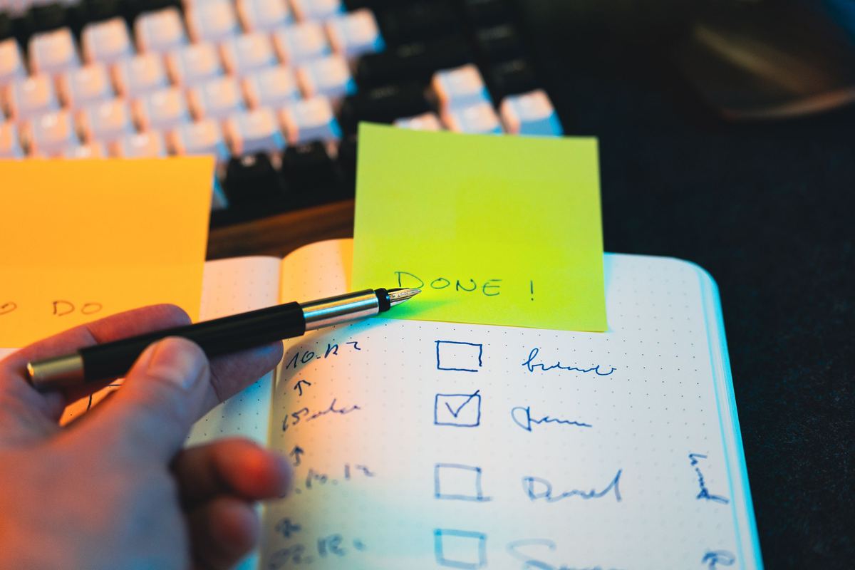 A hand writing a checklist in a notebook with sticky notes