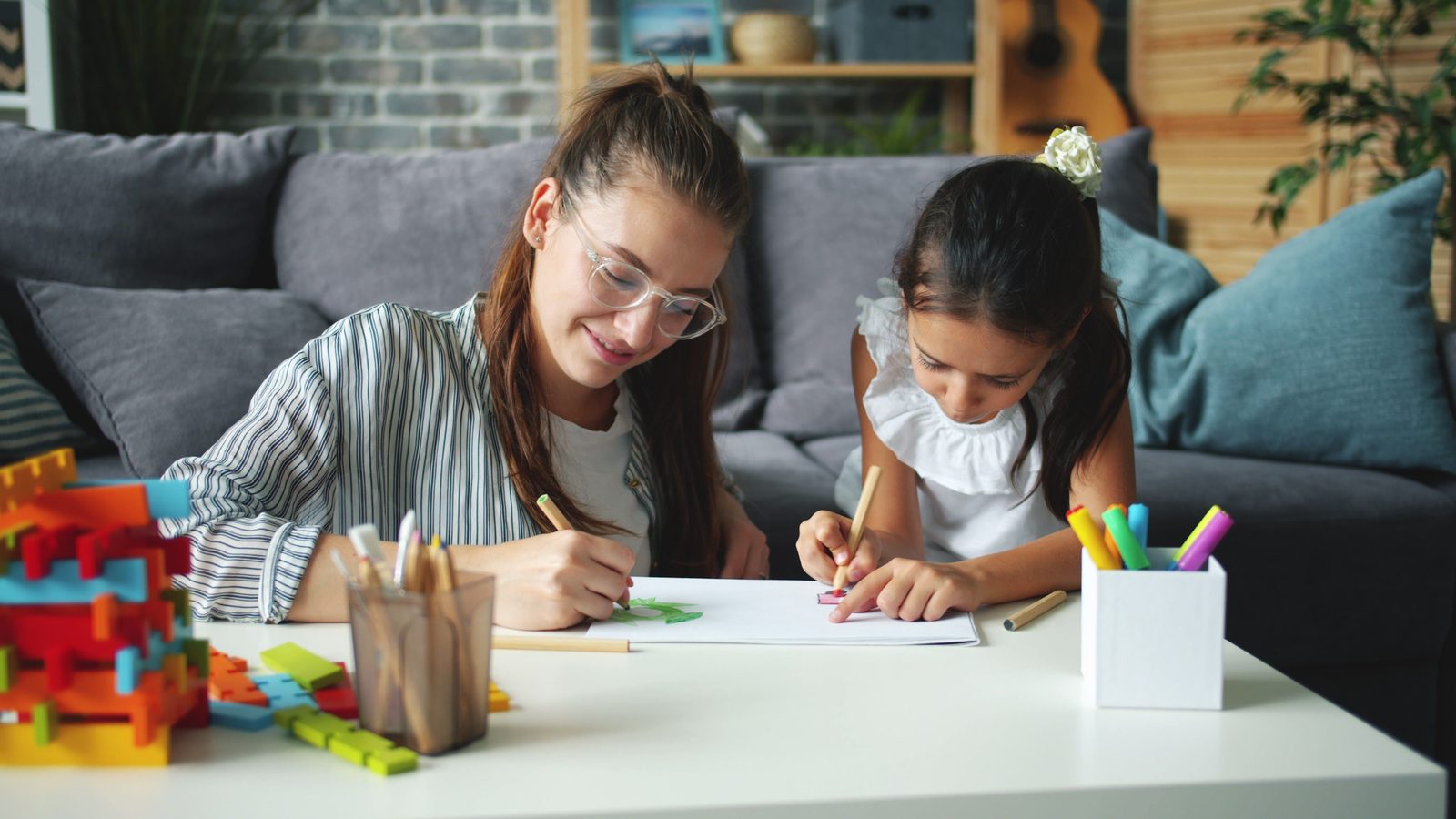 A child drawing with coloured pencils at a table in a bright, calm room
