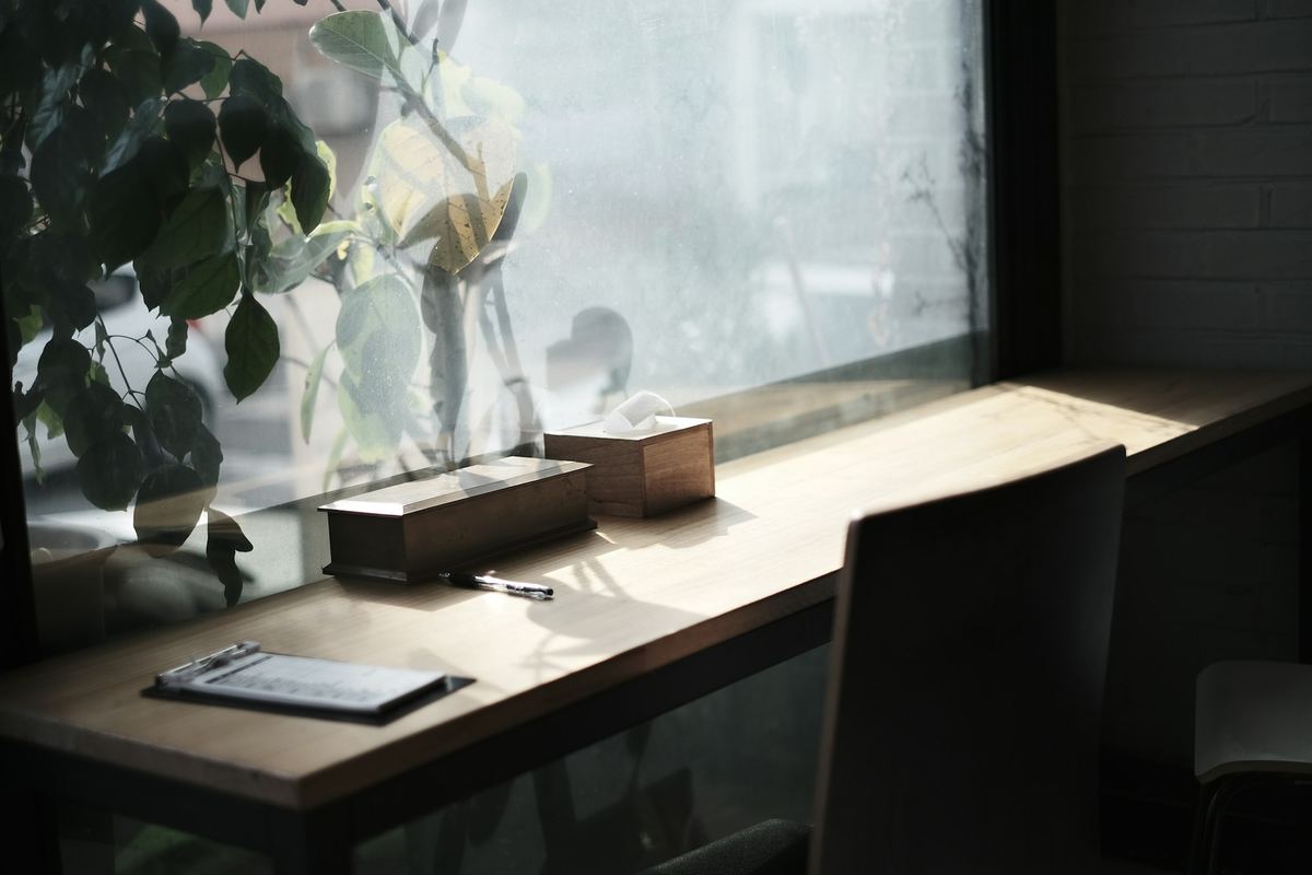 A wooden desk with a clipboard and pen beside a window