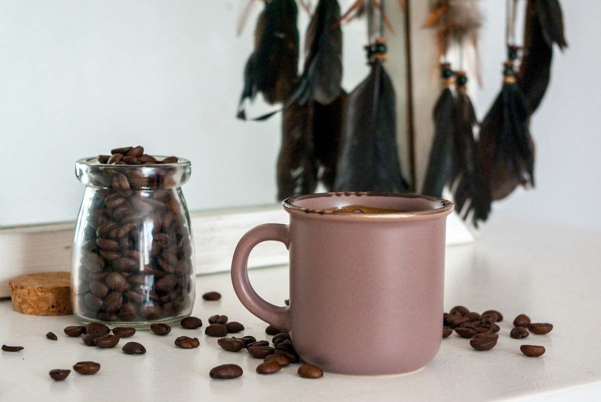 A ceramic mug of coffee beside scattered coffee beans
