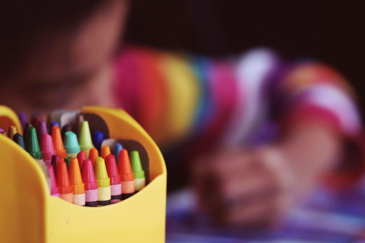 A child reaching into a box of coloured crayons