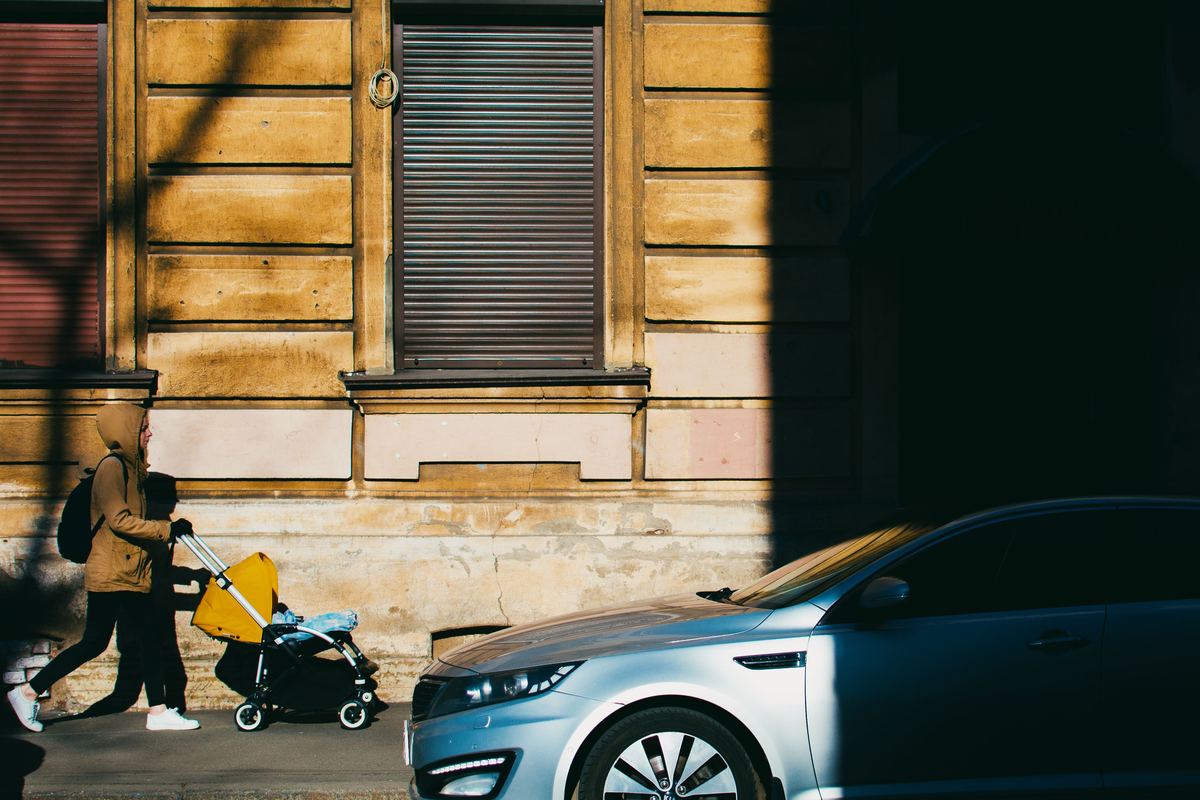 A person pushing a pram along a sunlit pavement