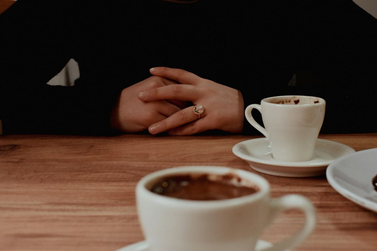 Hands clasped on a table beside two cups of coffee