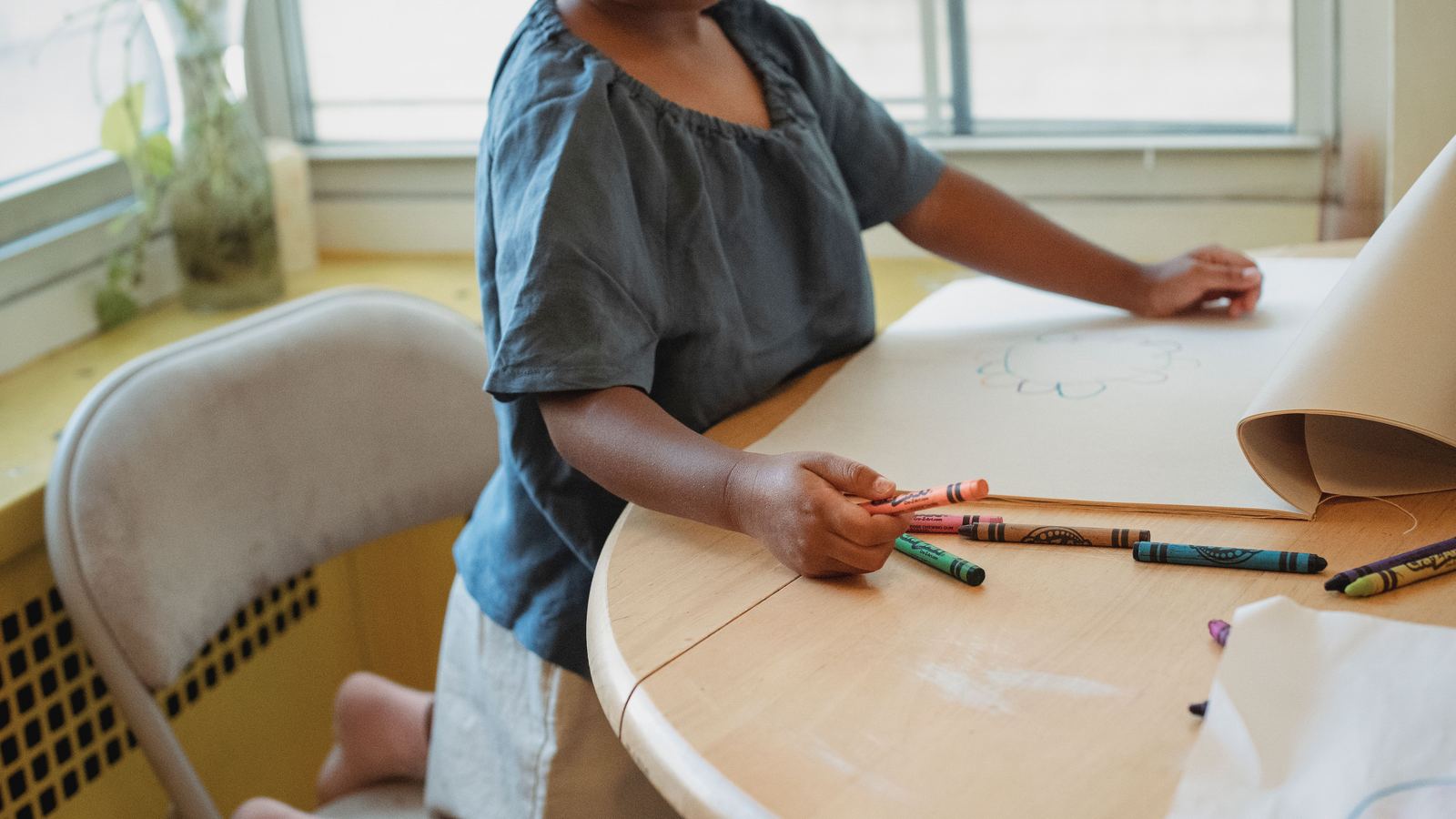A child drawing with crayons at a table in daylight
