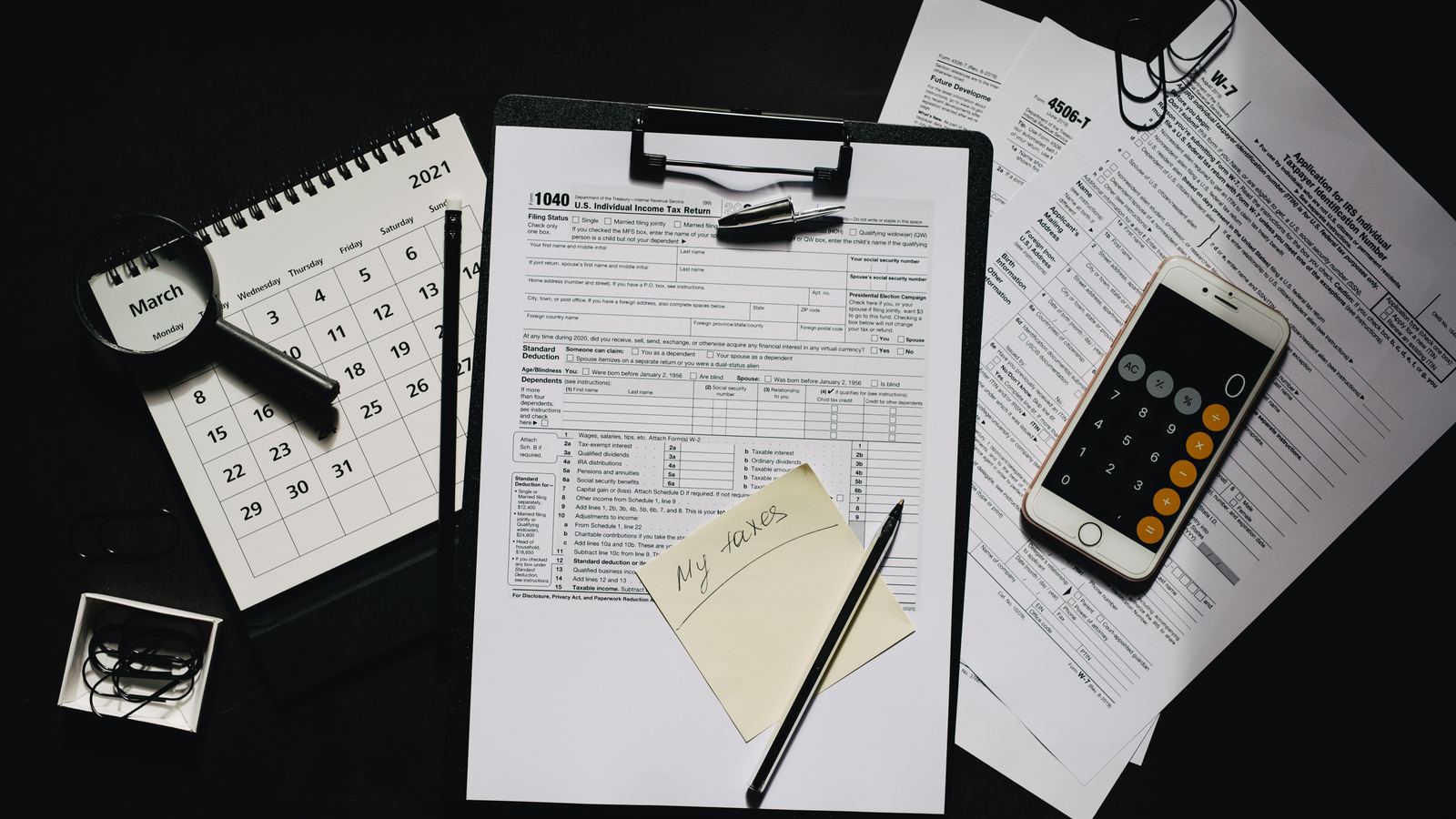 Forms, a calculator, a calendar and a pen laid out on a desk
