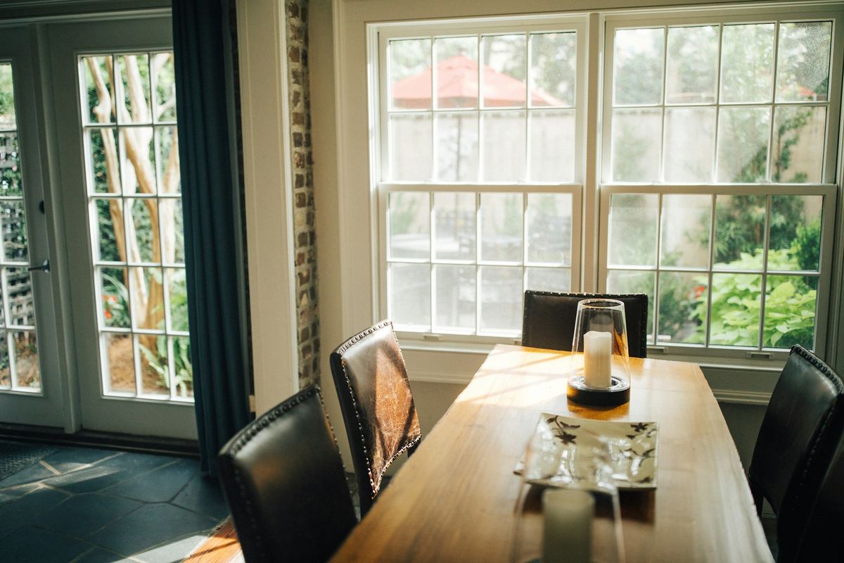 A wooden dining table and chairs beside bright windows