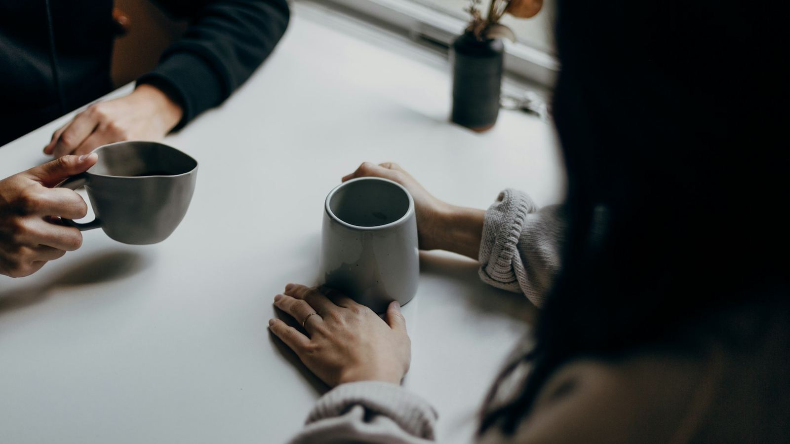 Two people holding mugs across a table