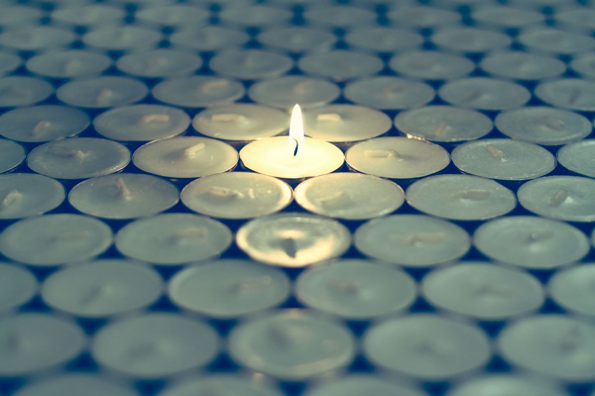A single lit tealight among unlit candles
