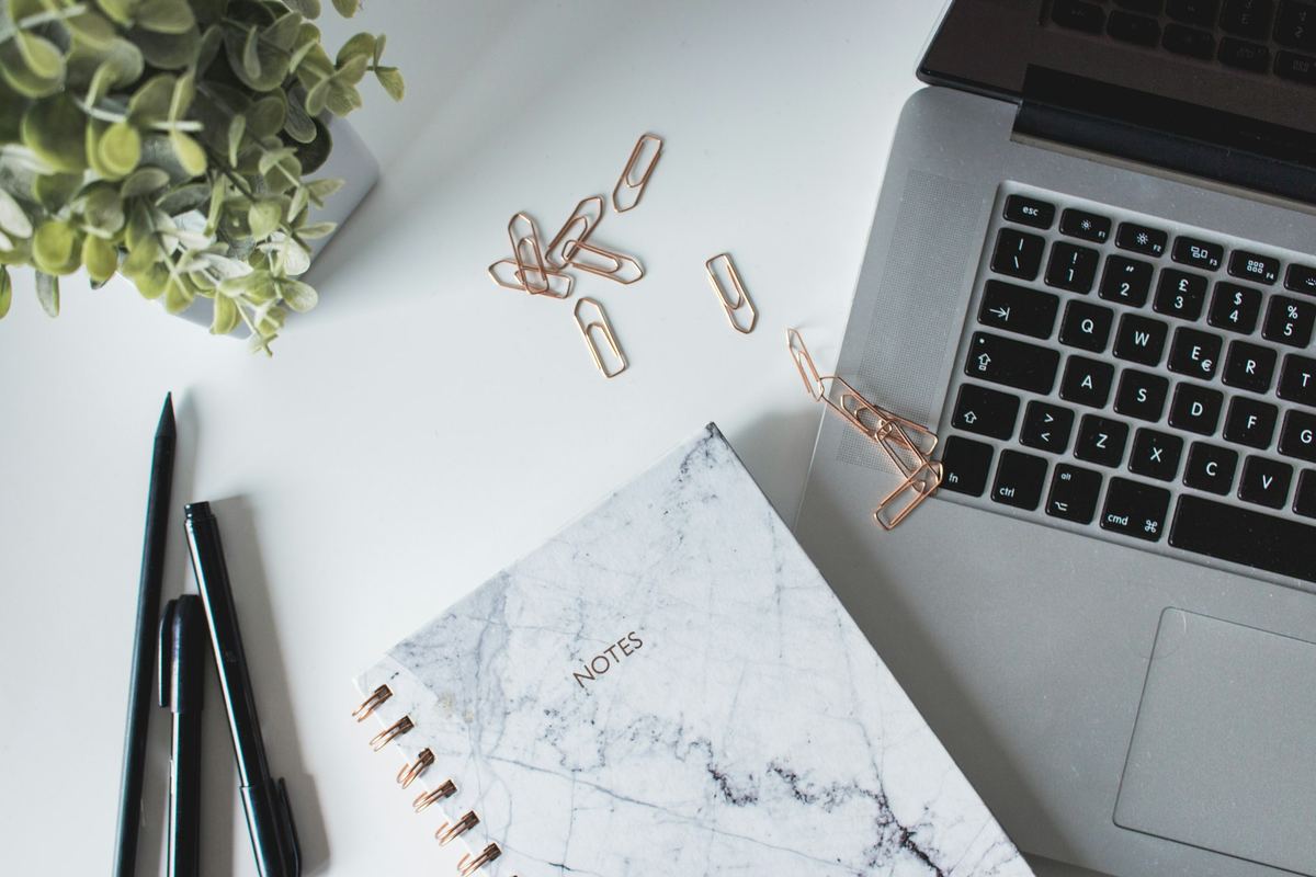 A laptop, notebook and pens arranged on a white desk