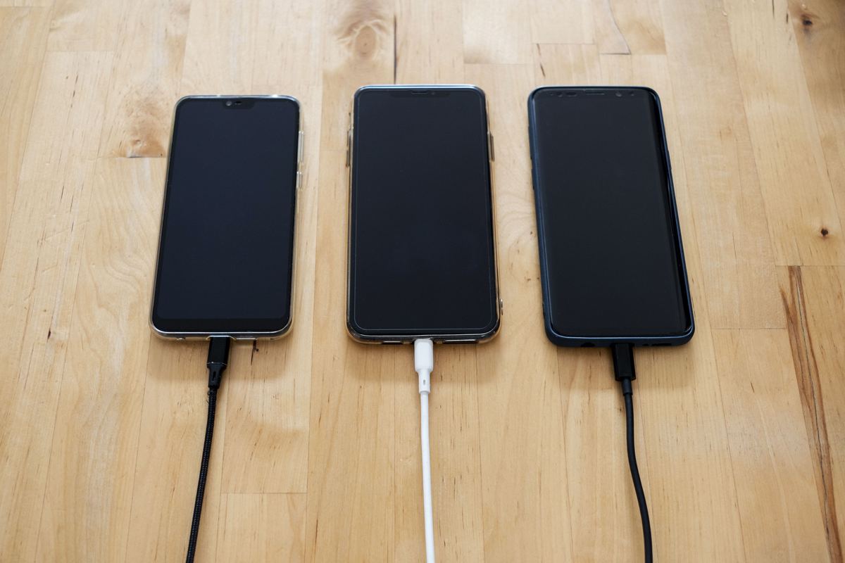 Three smartphones charging side by side on a wooden surface