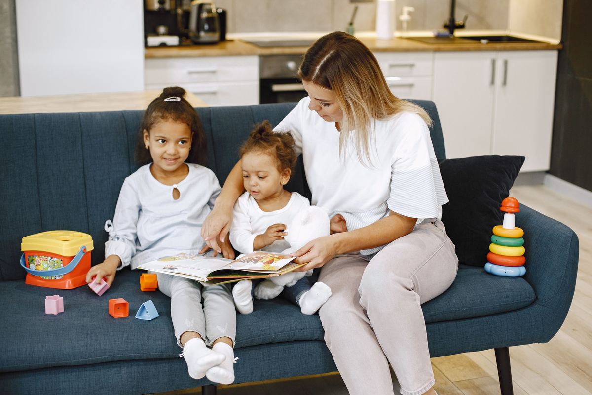 A parent reading a book with two children on a sofa