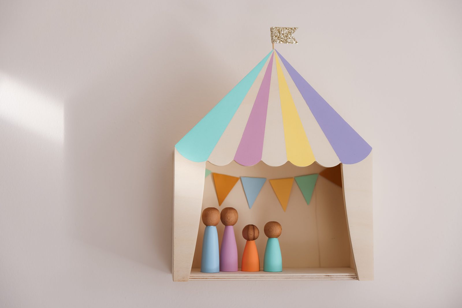 Small wooden peg figures standing inside a colourful toy tent