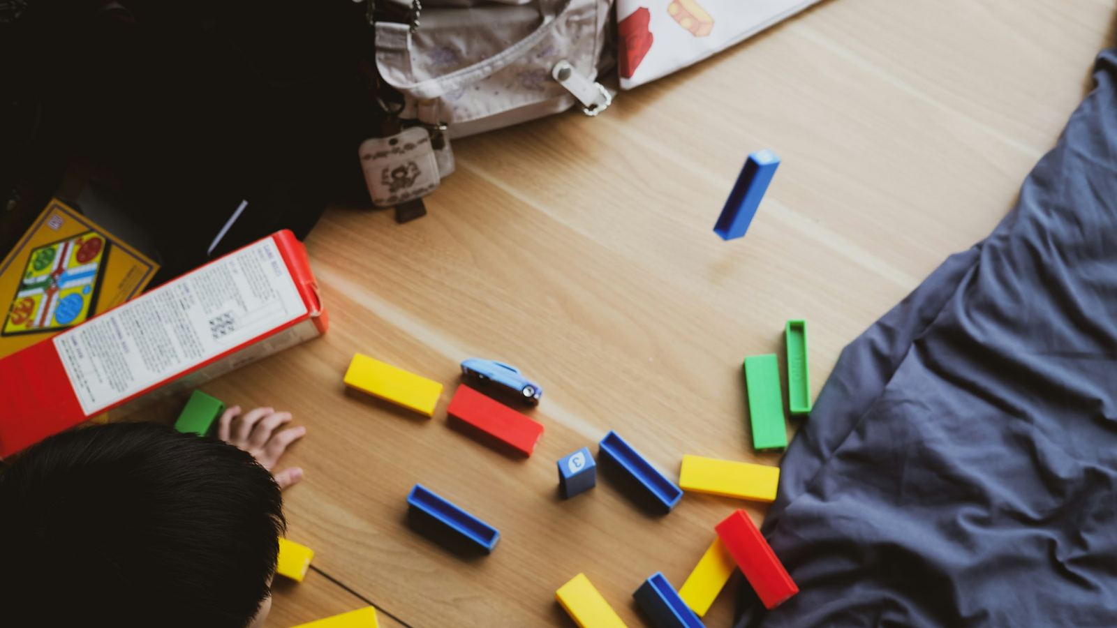 A child playing with colourful building blocks on a wooden floor