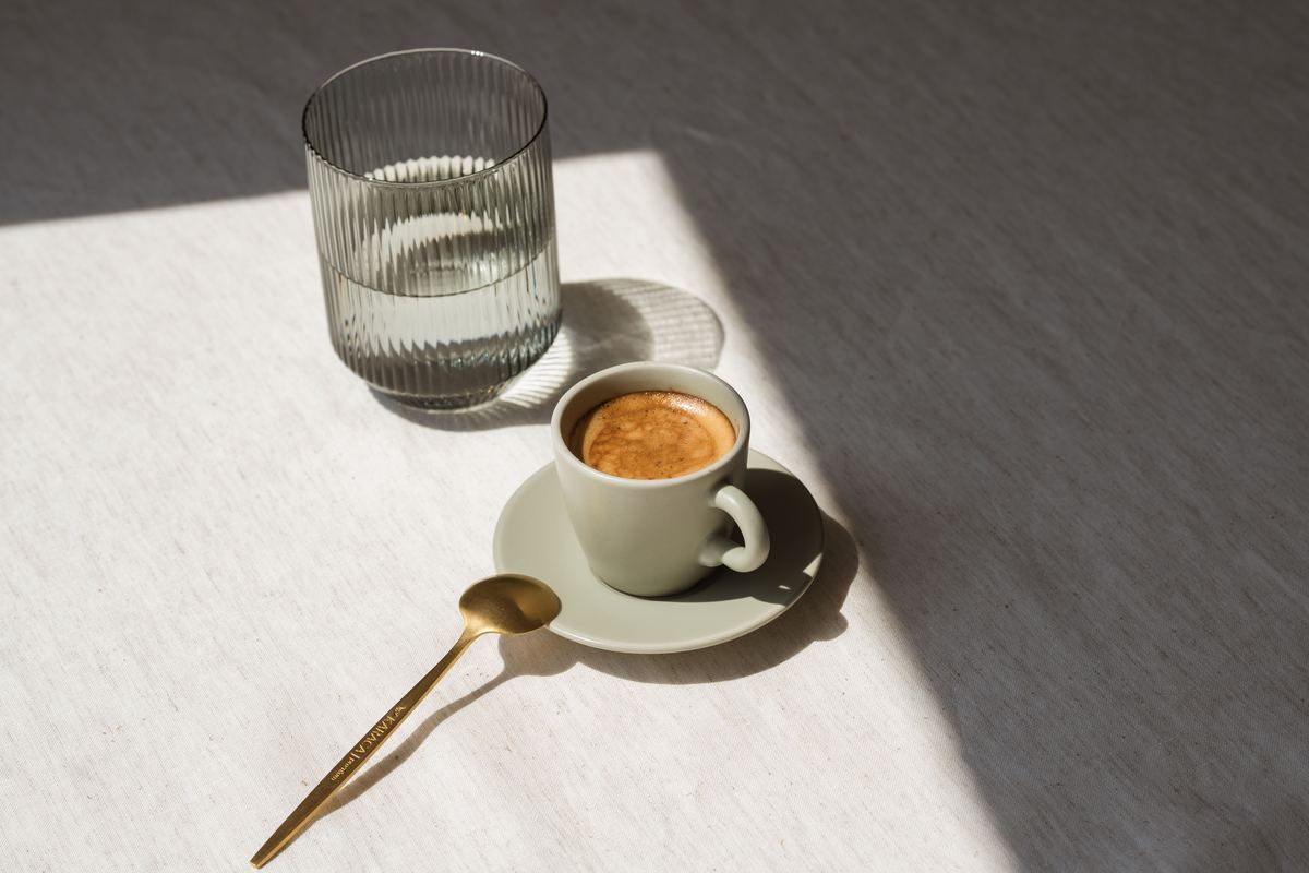 A coffee cup and a glass of water on a table in sunlight