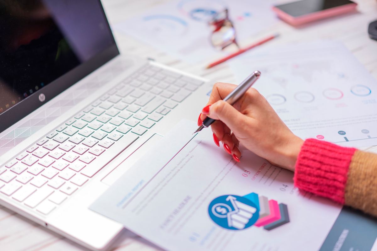 A person reviewing financial charts on a laptop and paper
