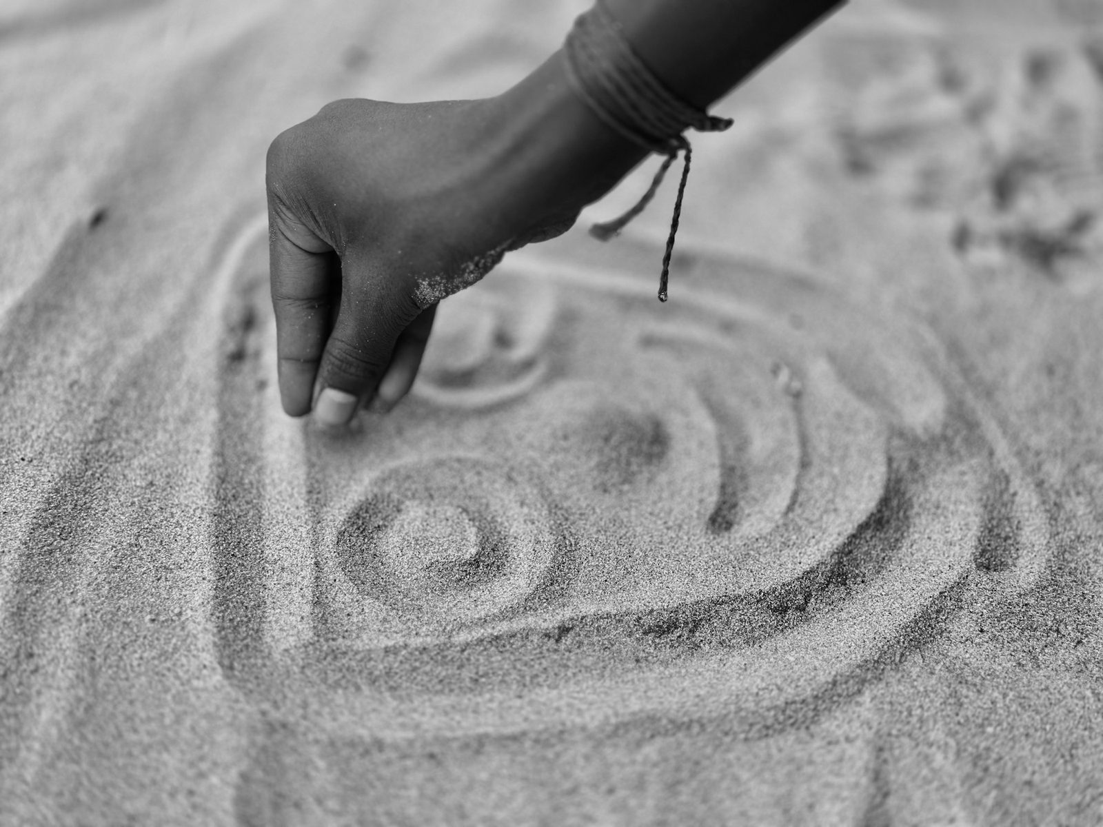 A hand tracing a spiral pattern in smooth sand