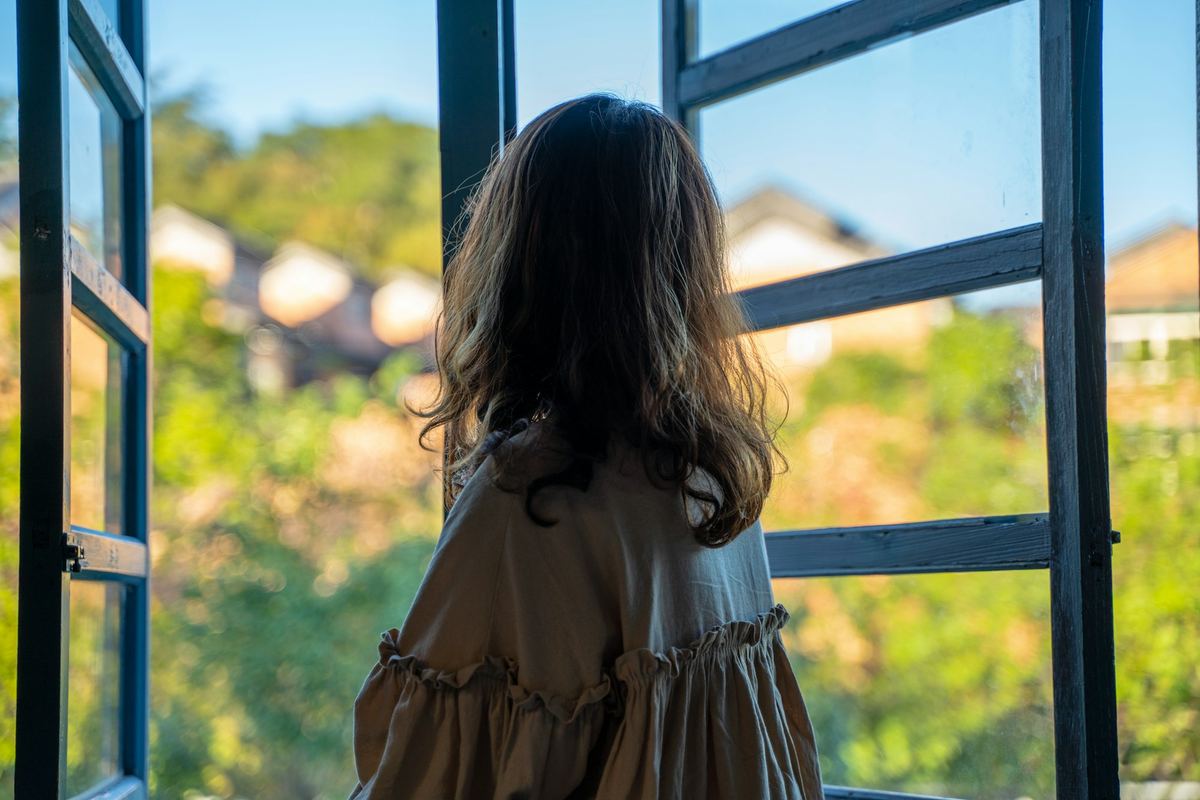 A young person standing outdoors beside a fence in daylight