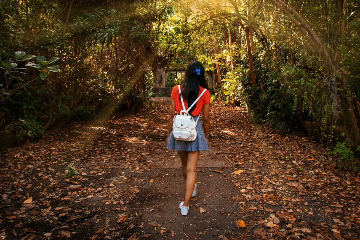 A young person walking along a leafy path with a backpack