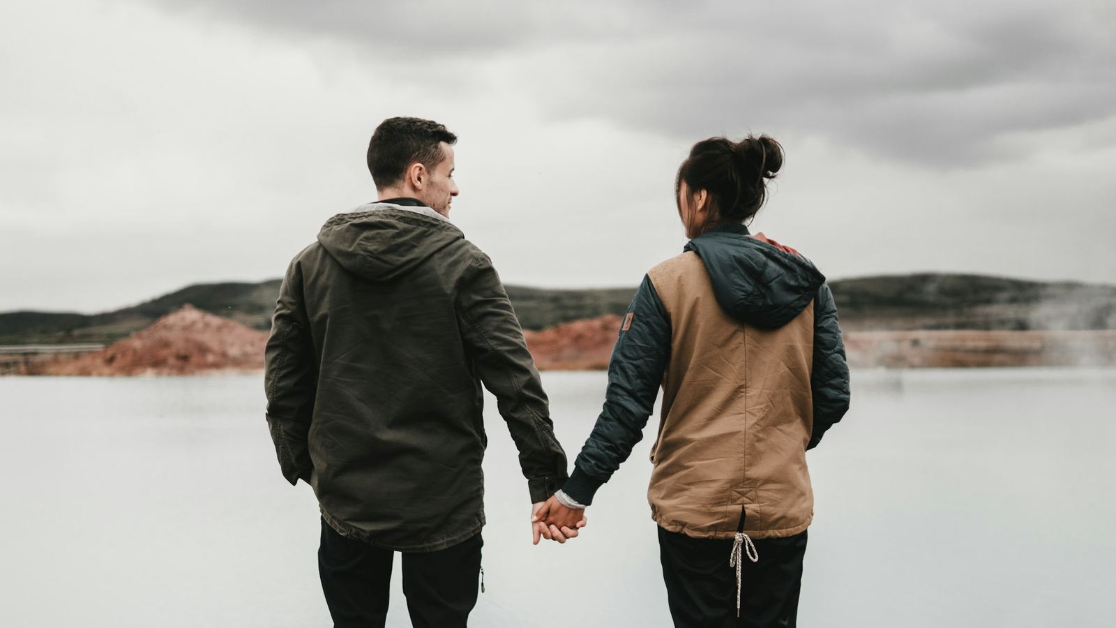 A couple holding hands looking out over calm water toward distant mountains