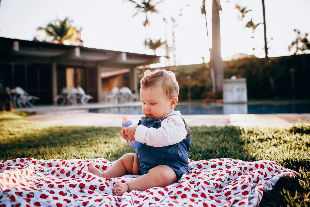 A baby sitting on a blanket outdoors on a sunny day