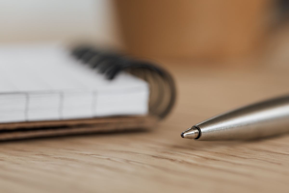 An open ring-bound notebook with blank pages beside a pen