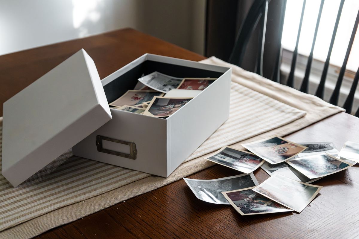 An open box of old family photographs on a table by a window