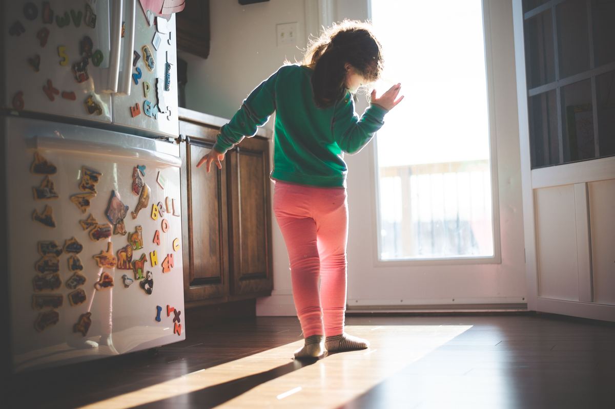 A child standing in a sunlit kitchen beside a fridge