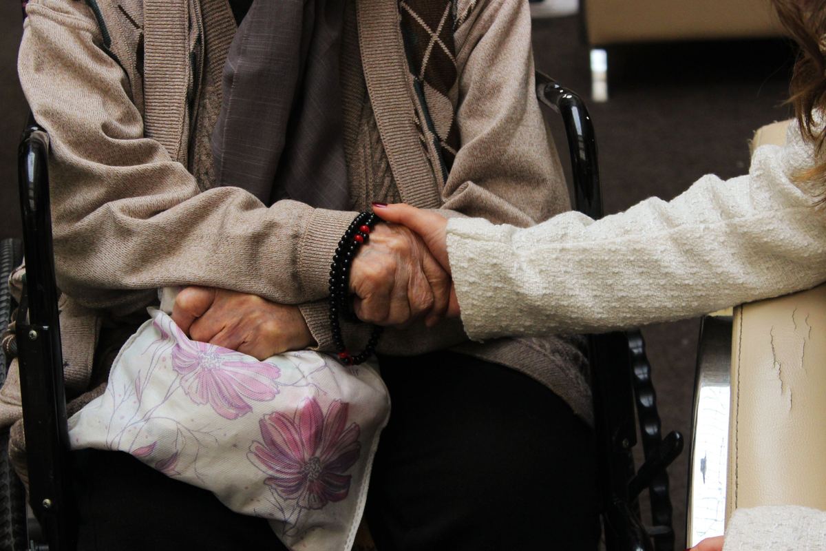 An older person in a wheelchair holding another person's hand