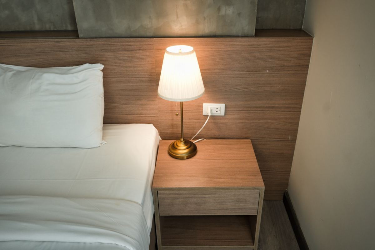 A bedside lamp lit on a wooden nightstand