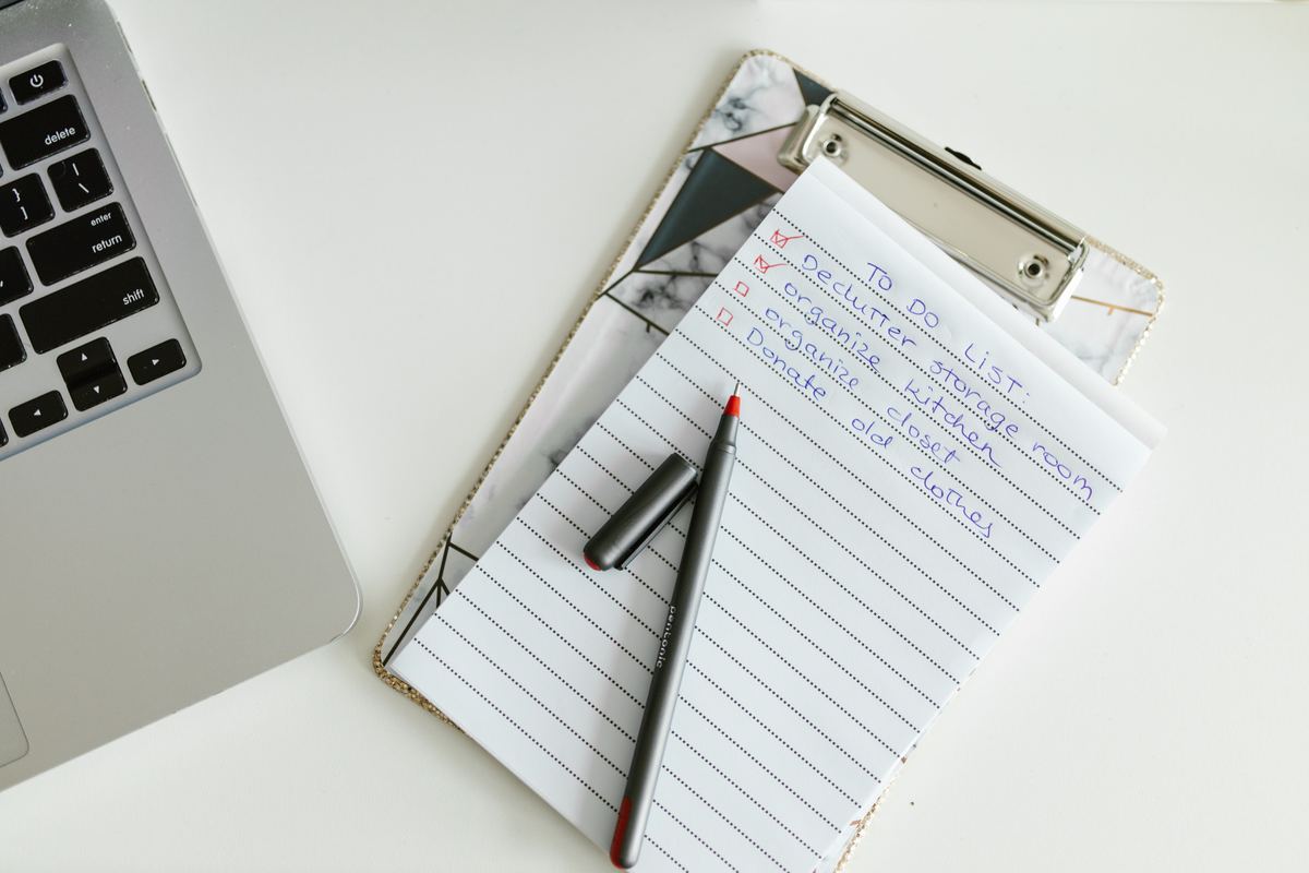 A handwritten to-do list on a clipboard beside a laptop
