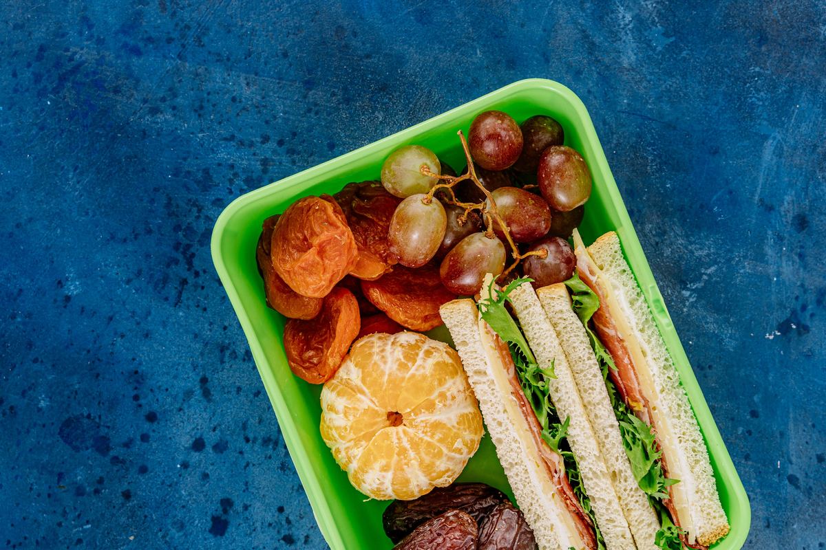 A lunch box packed with a sandwich, grapes and an orange