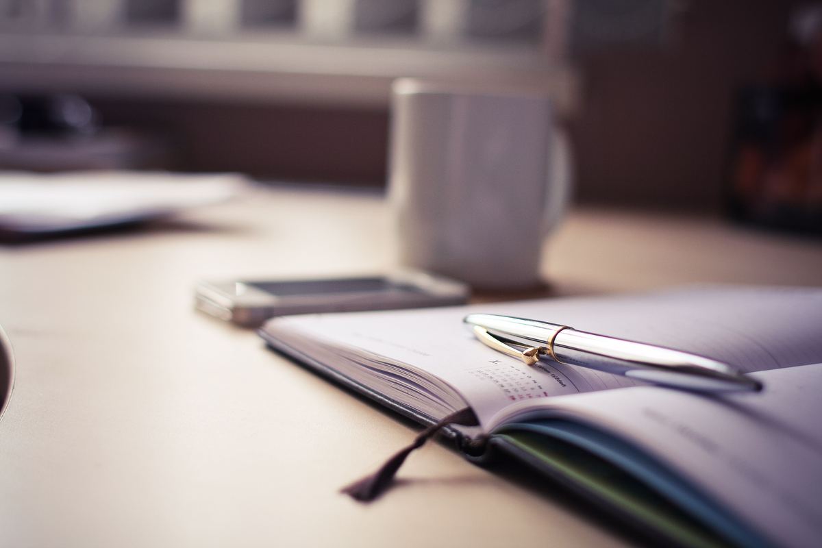 An open paper planner with a pen and a mug on a desk