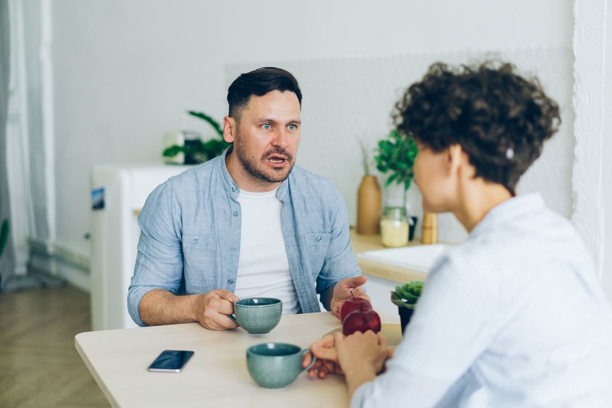 A couple talking across a kitchen table with coffee