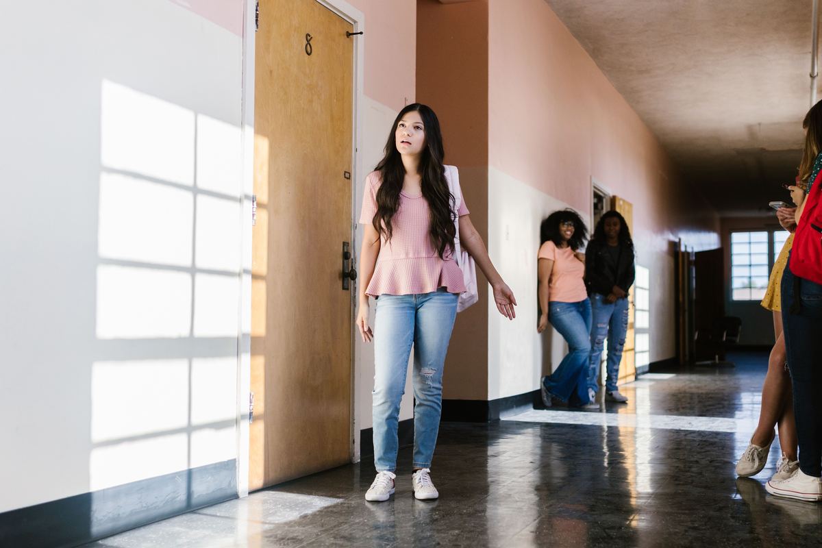 A teenager standing in a school corridor as other students pass