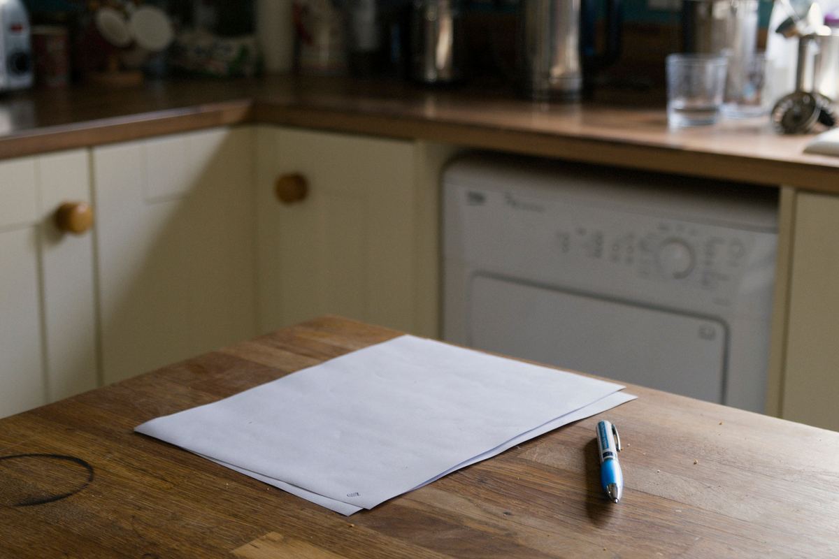 A blank sheet of paper and a pen on a wooden kitchen table