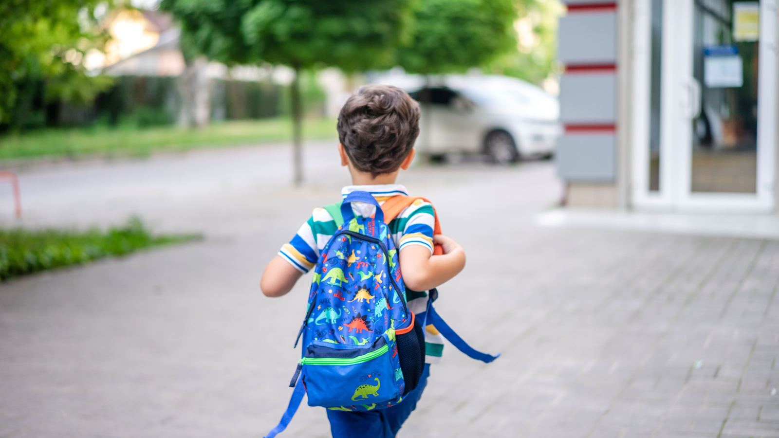 A child wearing a backpack walking along a sidewalk towards school