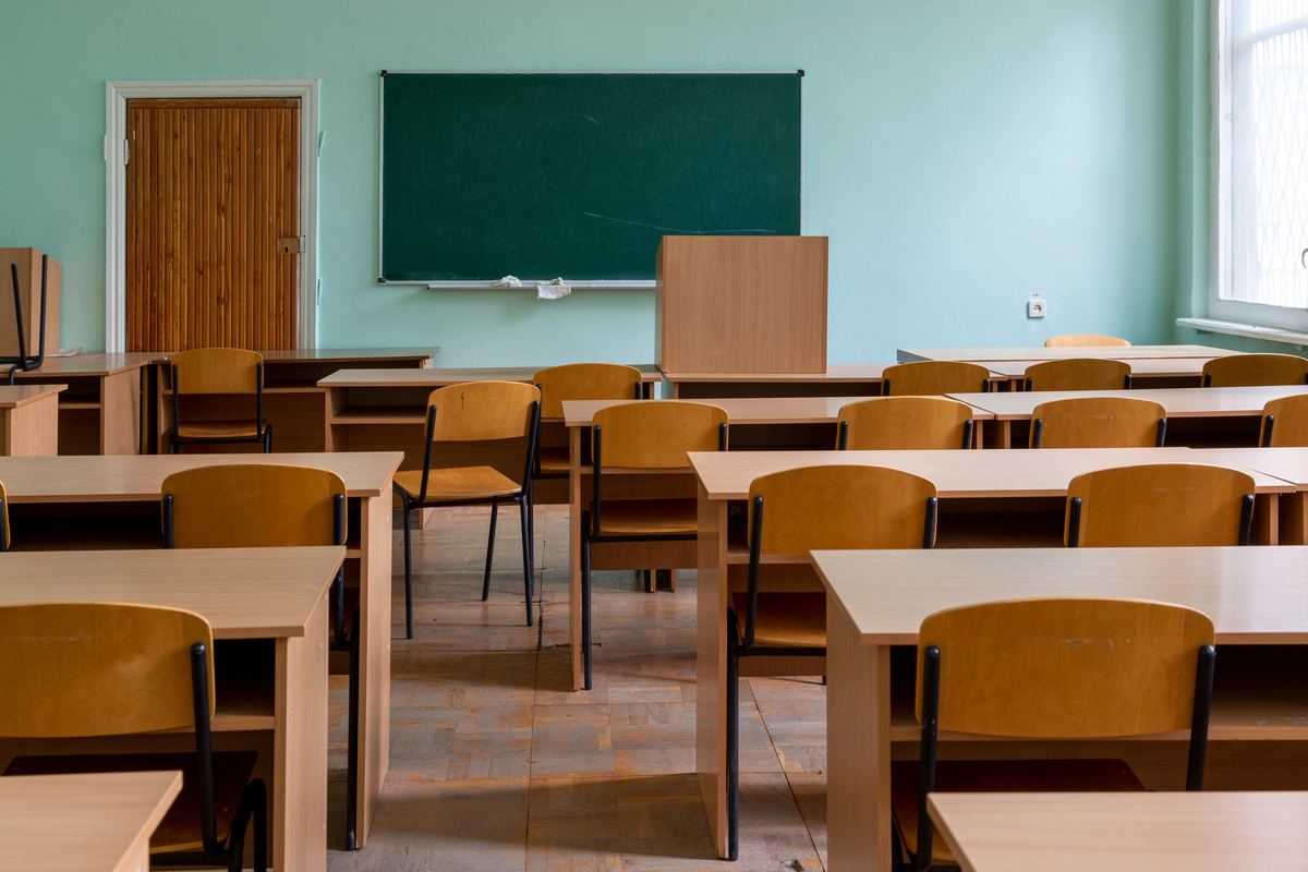 An empty classroom with wooden desks and a green chalkboard