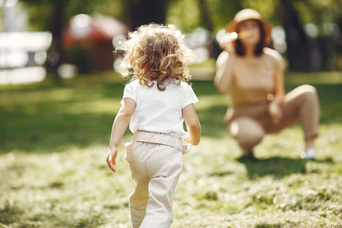 A parent crouching down as a child runs towards them in a park