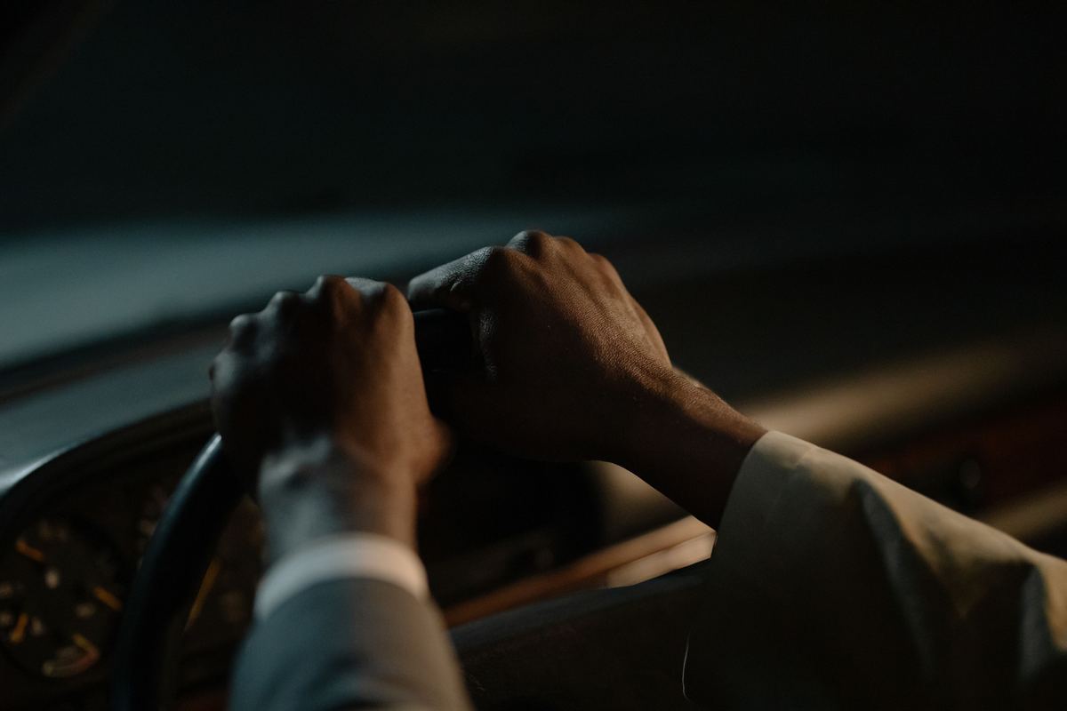 A driver's hands gripping a steering wheel in a dim car interior
