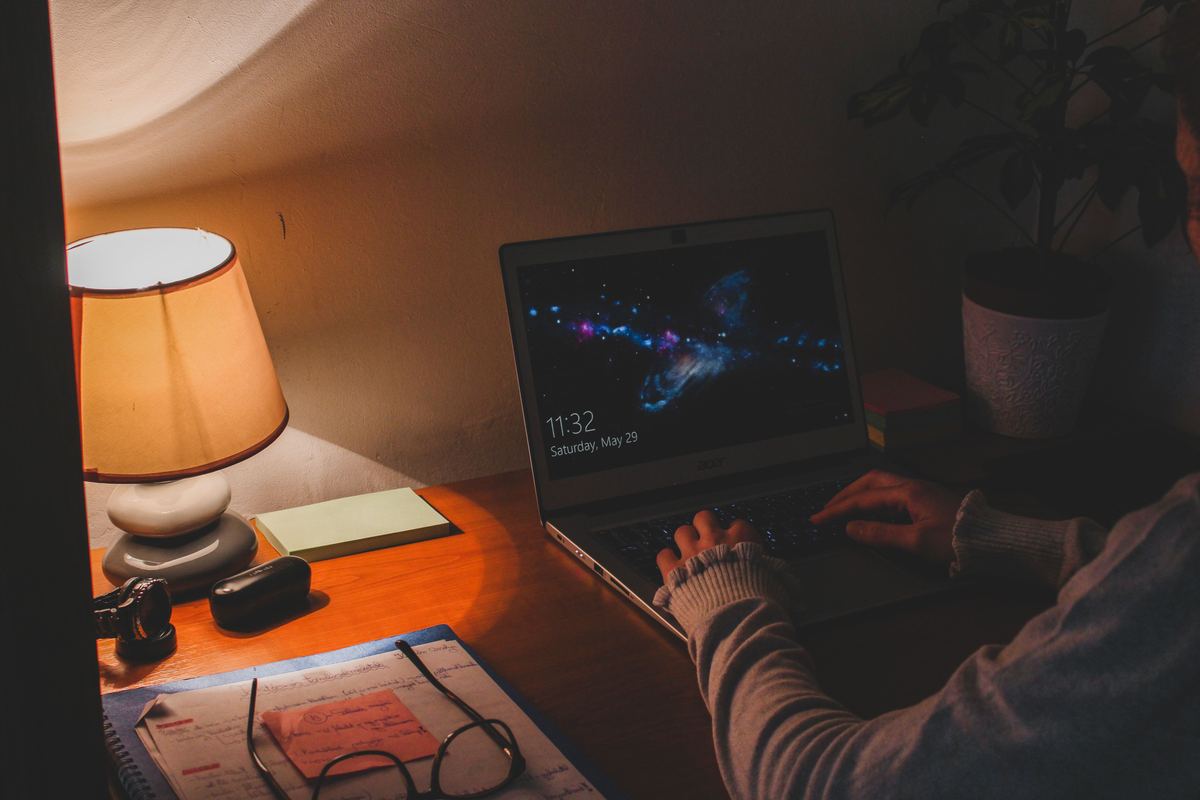 A desk lamp lighting a laptop and notebook late at night