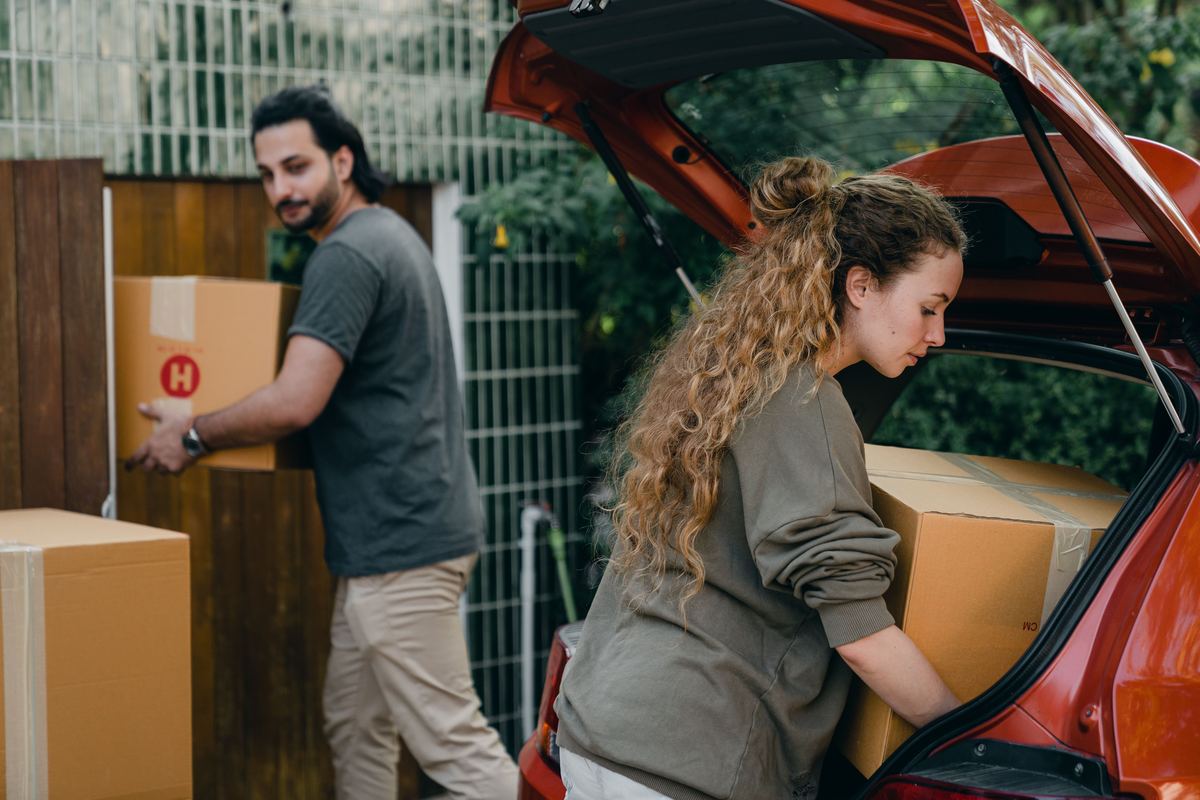 Two people loading boxes into the back of a car