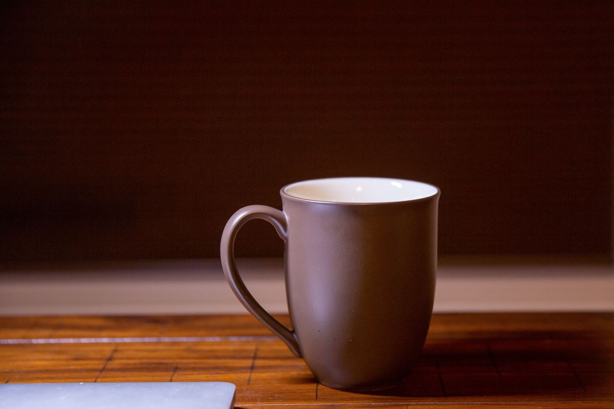 A single ceramic mug on a wooden table in low light