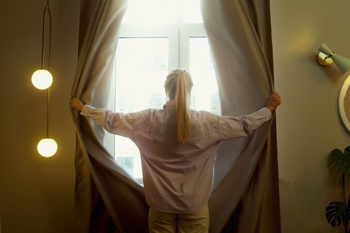 A person opening curtains in a softly lit room