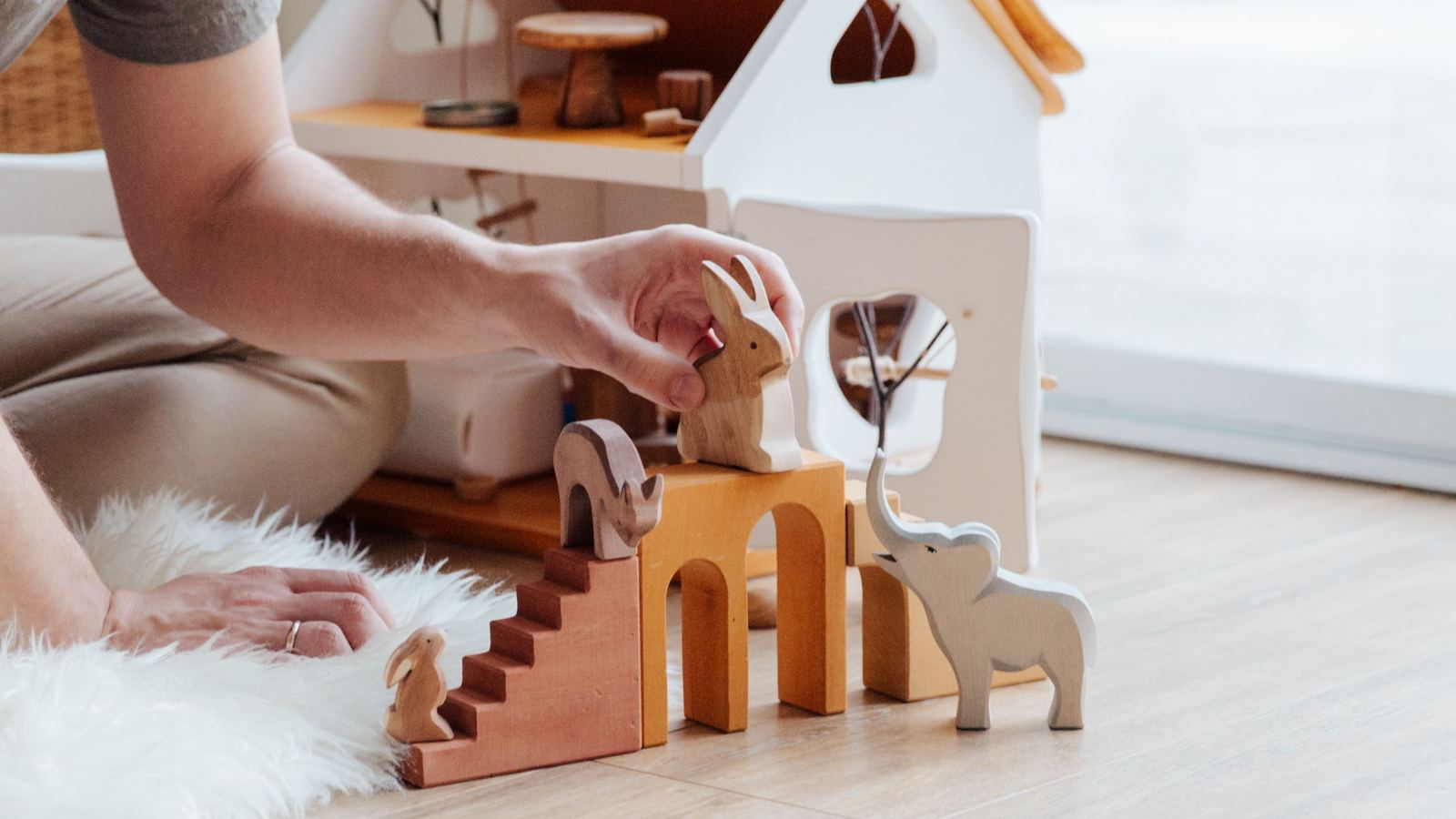 An adult hand placing a small toy figure beside a wooden dollhouse